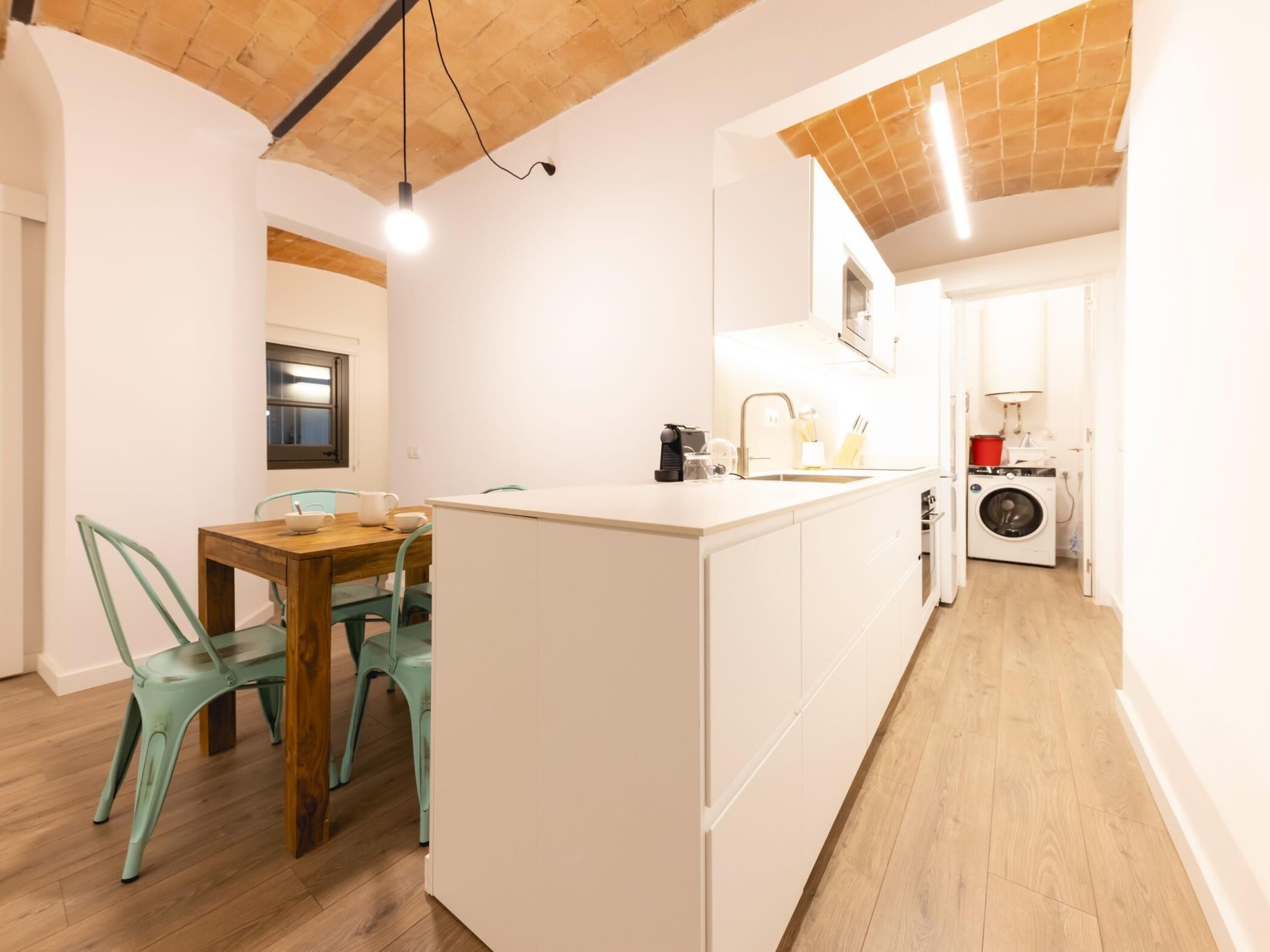 Une cuisine moderne avec un îlot central, un coin repas avec deux chaises et un lave-linge à l’arrière-plan.