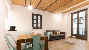 A modern living space with a wooden dining table, teal chairs, a grey sofa, and a small round table with a white wire basket.