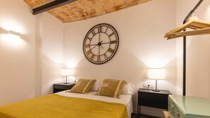 A bedroom with a large wall clock, two bedside tables with lamps, a bed with a yellow blanket, and a green dresser.