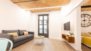 A modern living room with a grey sofa, a round coffee table, and a TV on a wooden shelf.