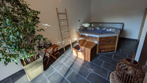 Un área de spa con una bañera de hidromasaje, mobiliario de madera, una escalera y una planta en maceta.