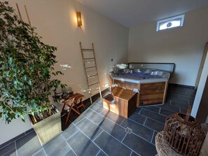 A spa area with a hot tub, wooden furniture, a ladder, and a potted plant.