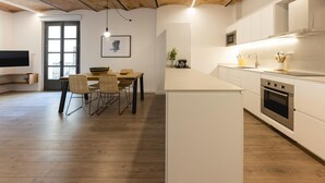 Una cocina moderna con armarios blancos, horno empotrado y zona de comedor con mesa y sillas.