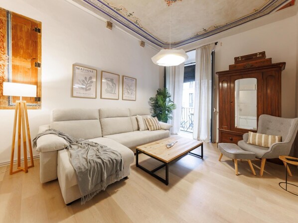 A living room with a sofa, a coffee table, a chair, and a lamp. There are framed pictures on the wall and a large mirror. - Bravissimo Plaça del Vi, Authentic and Historic in the Barri Vell (Girona)