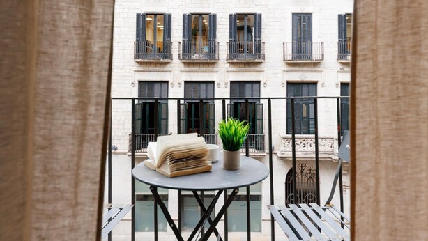 A balcony with a round table, a potted plant, and a stack of books. - Bravissimo Plaça del Vi, Authentic and Historic in the Barri Vell (Girona)