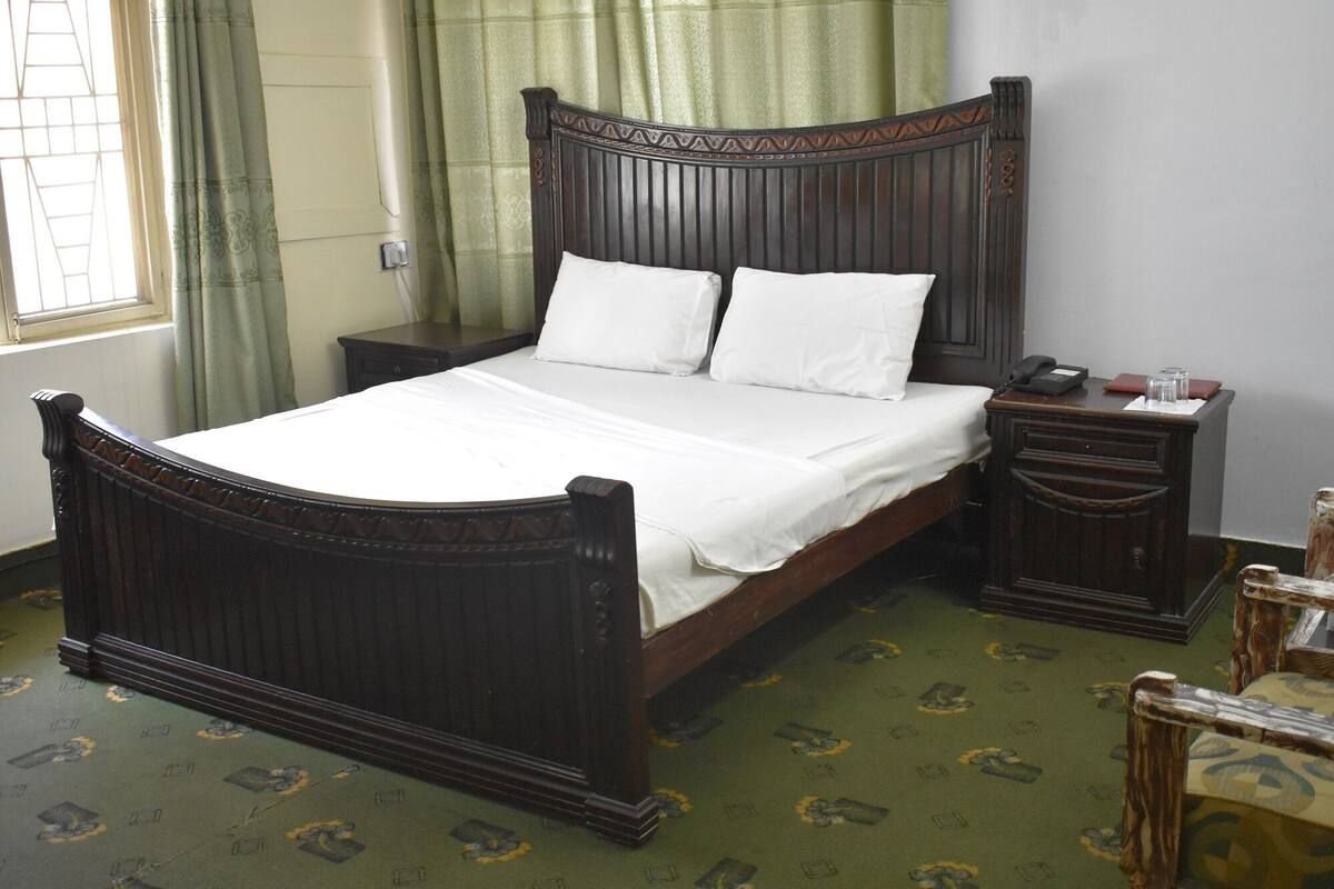 A traditional wooden four-poster bed with white linens, a nightstand, and a bedside table with a lamp.