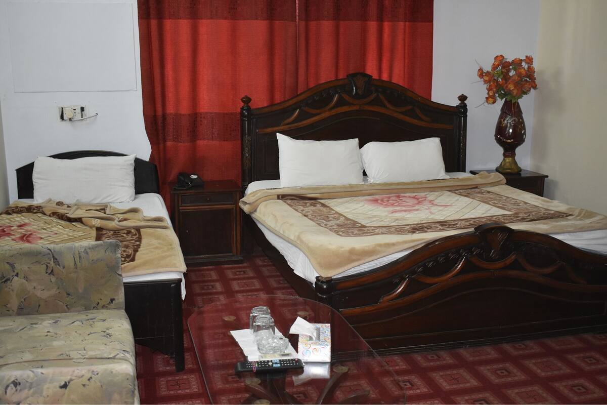 A hotel room with a large bed, a smaller bed, a sofa, a nightstand, a vase with flowers, and a carpeted floor.