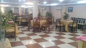 A dining area with checkered flooring, multiple tables, and chairs. - Savvana Inn (Islamabad)