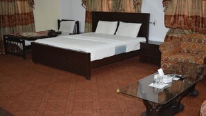 A hotel room with a large bed, a bedside table, a glass coffee table, and a patterned carpet. - Savvana Inn (Islamabad)