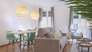 A modern living room with a sofa, a dining table with chairs, and a coffee table. There are two hanging lights and a window with curtains. - Bravissimo Sunset, comfort in the Old Town (Girona)