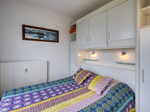 A bedroom with a bed, a white wardrobe, a framed picture on the wall, and a radiator.