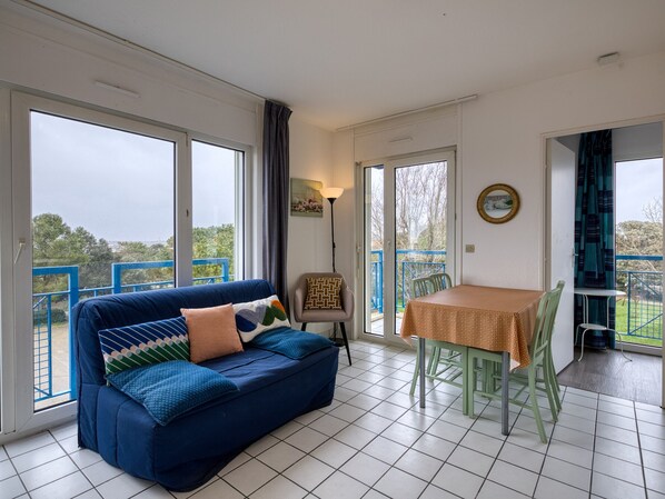 A room with a blue sofa, a table with chairs, and large windows.