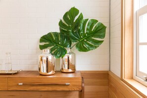 Uma cômoda de madeira com dois vasos de vidro contendo plantas monstera verdes.