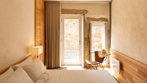 A bedroom with a bed, a chair, a lamp, and a view of a stone wall through a door. - Garden of Camellias ★ Charming house near beach (4 bedrooms) (Porto)