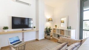 Ein modernes Wohnzimmer mit Flachbildfernseher, Laptop, Sofa, Couchtisch, Lampe und Bücherregal.