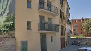 Eine enge Straße mit einem beigefarbenen Gebäude mit Balkonen und einem Wandgemälde auf der linken Seite.