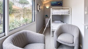 Una habitación con literas, un escritorio, dos sillones, un ventanal con vista a follaje y una lámpara fijada en la pared.