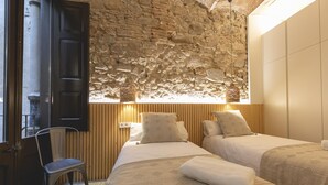 A room with two beds, a wooden wall, a stone wall, a chair, and a window. - Bravissimo Mercaders 3-1-2, unique and with 3 bedrooms in the historic center (Girona)