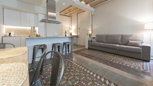 A modern kitchen with a central island, bar stools, and a grey sofa in a living area. - Bravissimo Mercaders 3-1-2, unique and with 3 bedrooms in the historic center (Girona)