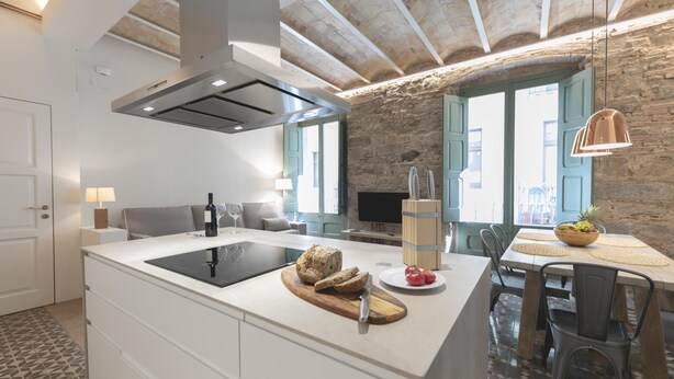 A modern kitchen with a central island, a built-in stove, and a stone wall. - Bravissimo Mercaders 3-1-2, unique and with 3 bedrooms in the historic center (Girona)