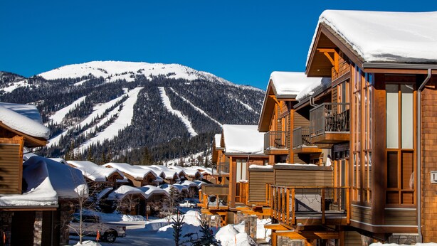 A snow-covered mountain resort with wooden buildings and a ski slope in the background. - Spacious multi level 4 bedroom + den townhouse, ski in/ski out (Sun Peaks)