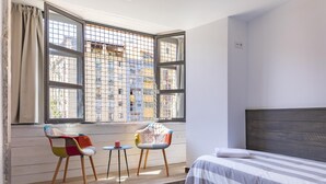 Ein Schlafzimmer mit einem Bett, einem Fenster mit Blick auf Gebäude, einem kleinen Tisch und zwei Stühlen.
