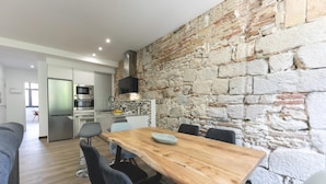A modern kitchen with a stone wall, a dining area with a wooden table and chairs, and a visible refrigerator. - Bravissimo Rambla Eiffel 2, 3 bedrooms, located next to the Eiffel Bridge (Girona)
