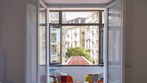 A room with a bed, a small table, and two colorful chairs. A window reveals a view of buildings and a red-roofed street. - Bravissimo Rambla Eiffel 2, 3 bedrooms, located next to the Eiffel Bridge (Girona)