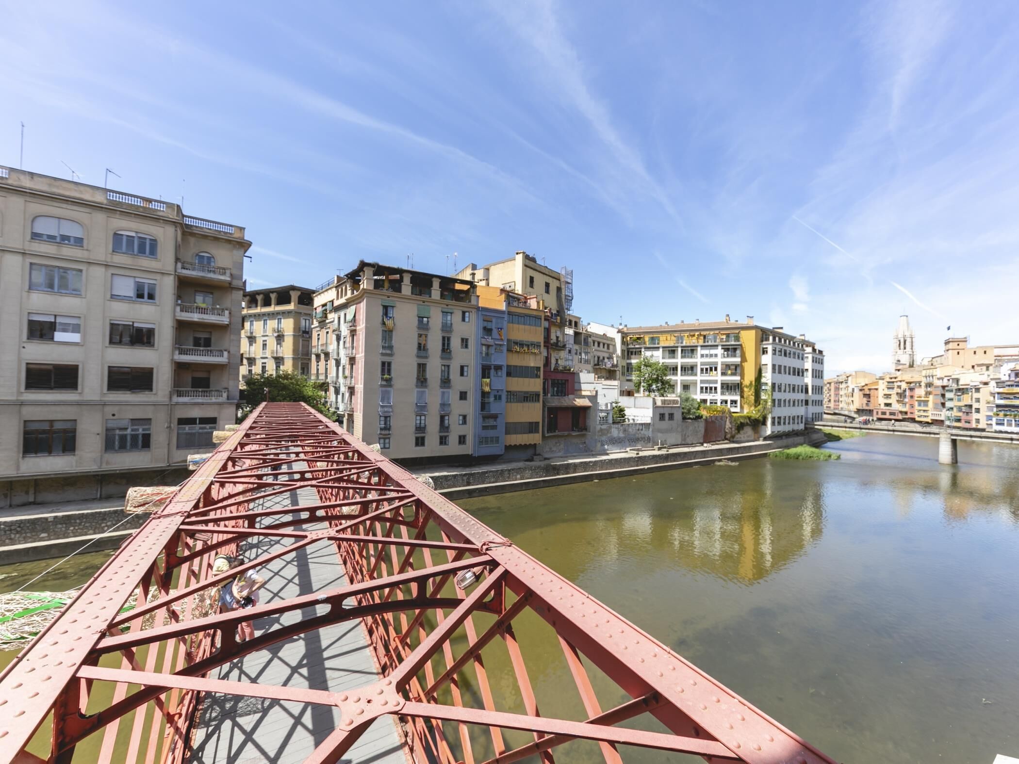 A red metal bridge over a calm river with buildings on either side.