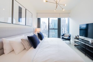 A modern hotel room with a large bed, a TV, a chair, and a city view. - EDEN'S Homes & Villas - BLVD Heights (Dubai)
