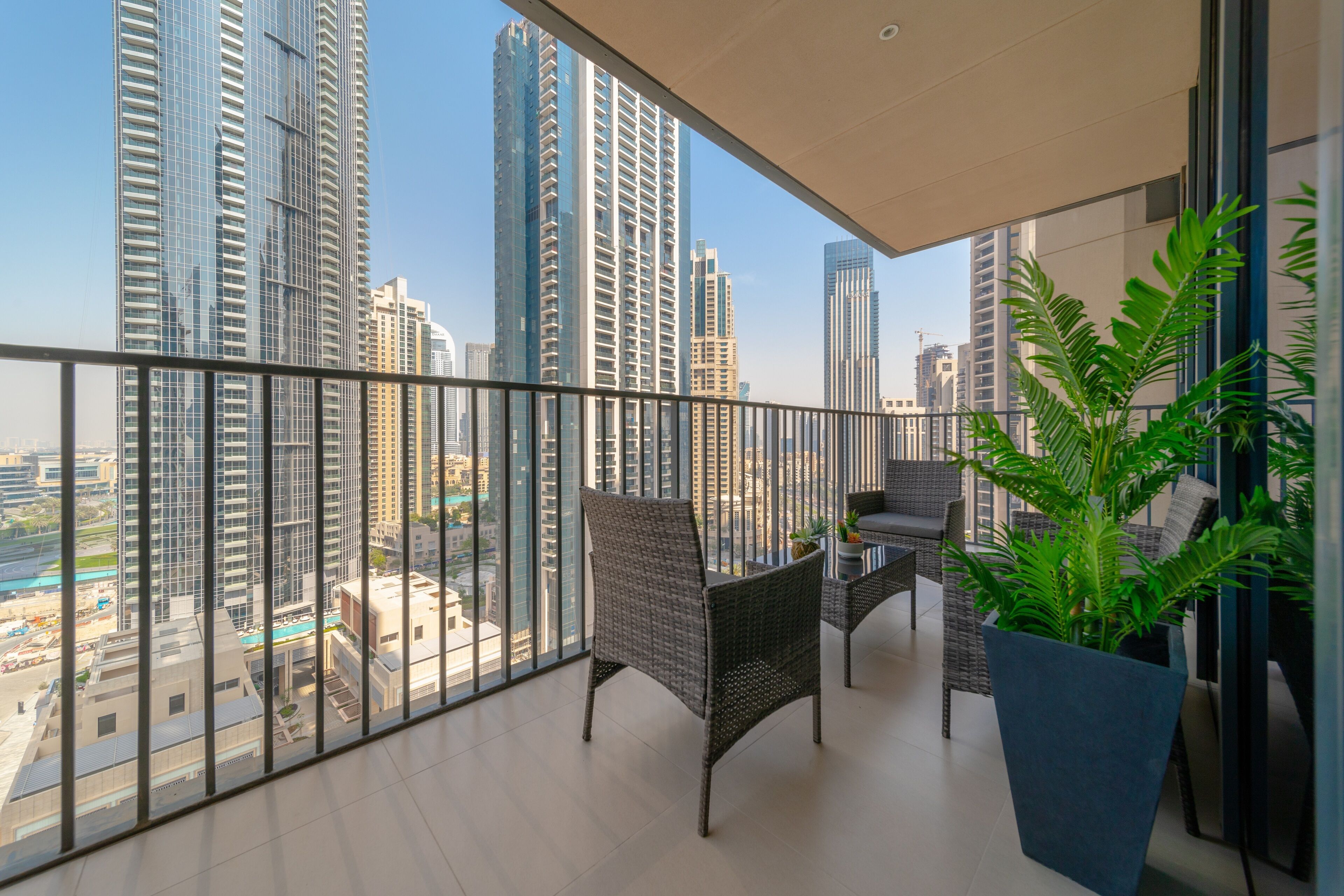 Ein Balkon mit Korbmöbeln, einem Topfpflanzen und Blick auf hohe Gebäude.