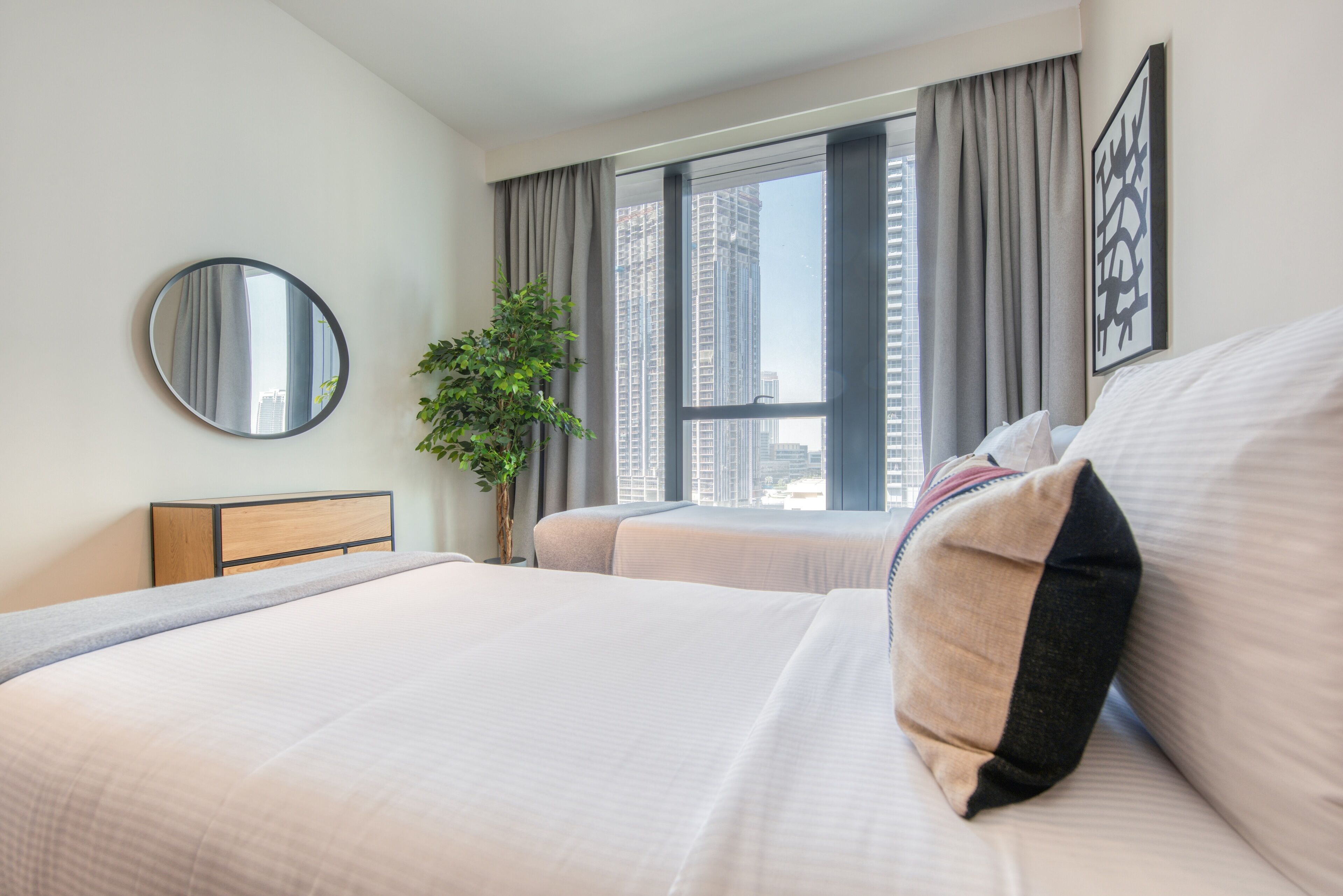 Ein Hotelzimmer mit einem großen Bett, einem Nachttisch, einem Spiegel, einem Fenster mit Vorhängen und Blick auf hohe Gebäude.