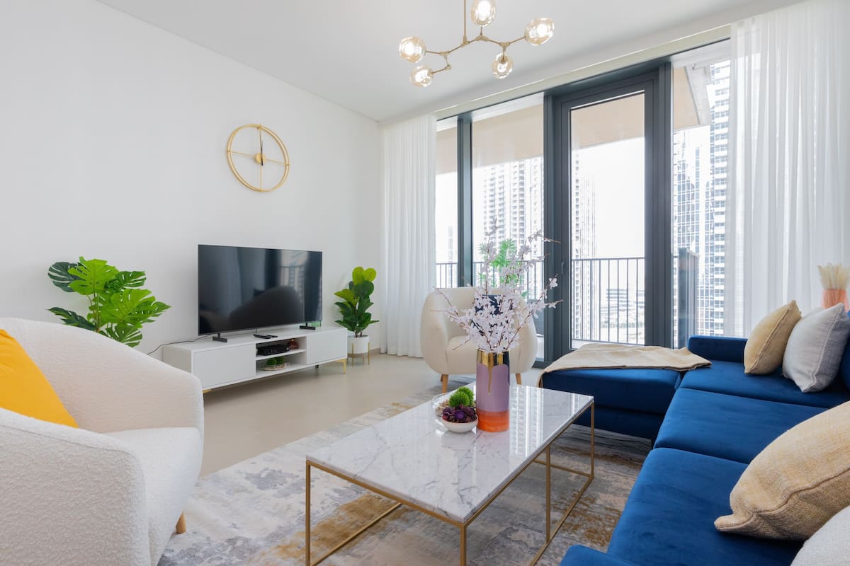 A modern living room with a large TV, comfortable seating, and a view of the city through large windows.