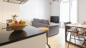 A modern kitchen with a central island, a grey sofa, and a dining area with a table and chairs. - Bravissimo Bali, beautiful 2-bedroom apartment (Girona)