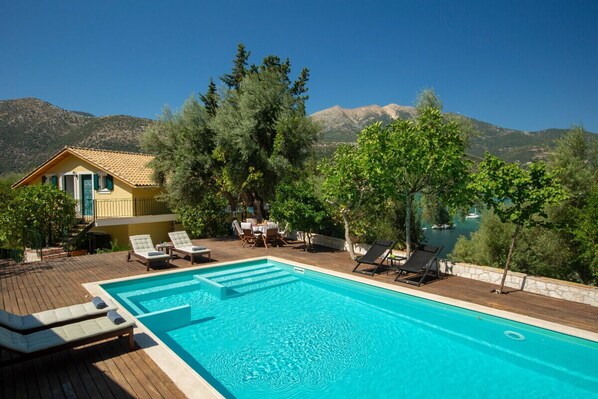 A swimming pool with lounge chairs, a wooden deck, and a mountain backdrop.