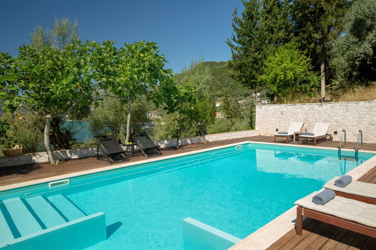 Une piscine d’un bleu éclatant, avec des chaises longues et un mur de pierre en arrière-plan.