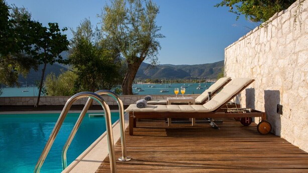 A wooden deck with a pool, lounge chairs, and a stone wall. - Liana's House with great view in Vlicho Bay & big private pool ! (Lefkada)
