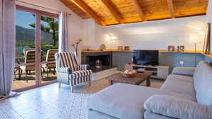A living room with a fireplace, sofa, television, and a view of the outdoors. - Liana's House with great view in Vlicho Bay & big private pool ! (Lefkada)