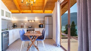 A modern kitchen with wooden ceiling, a dining table with blue chairs, and a view of mountains through large windows. - Liana's House with great view in Vlicho Bay & big private pool ! (Lefkada)