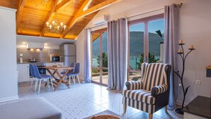 A cozy living room with a wooden ceiling, a dining area with blue chairs, and a view of a mountain through large windows. - Liana's House with great view in Vlicho Bay & big private pool ! (Lefkada)