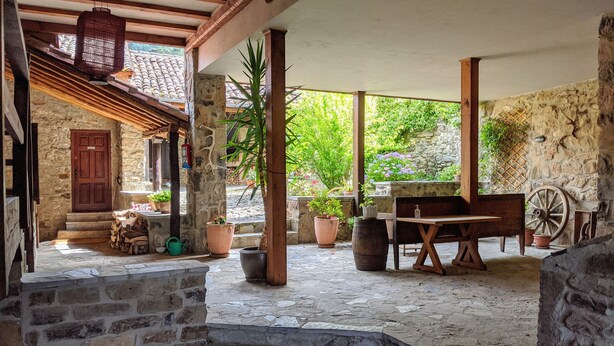 Un patio rústico al aire libre con paredes de piedra, vigas de madera y una escalera de piedra que lleva a una puerta de madera.