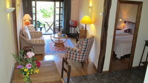 Una sala de estar acogedora con un sofá, un sillón y una mesa de comedor con un jarrón de flores. Se ve también un televisor y una lámpara.