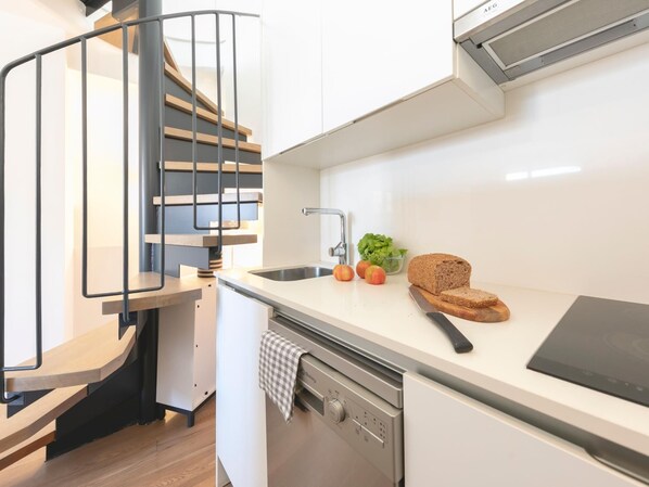 A modern kitchen with a built-in dishwasher, a stainless steel sink, and a black induction cooktop.
