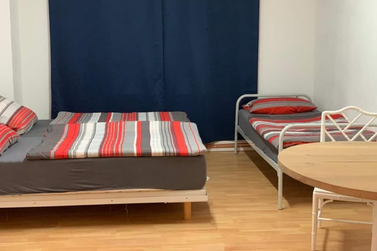 Een kamer met twee bedden, één groter en één kleiner, beide met streepjesbeddengoed. Er staat een houten tafel en een stoel in de kamer.