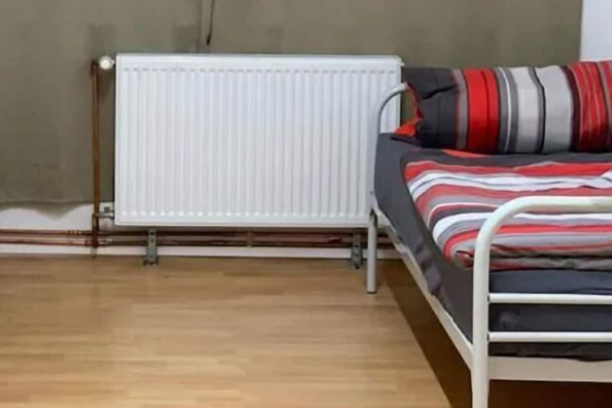 Een kamer met een radiator, een bed met gestreepte lakens en een houten vloer.