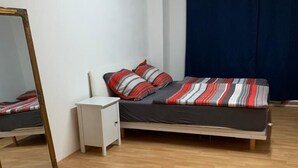 Een slaapkamer met houten vloer, een bed met gestreepte beddengoed, een witte nachtkastje en een spiegel.