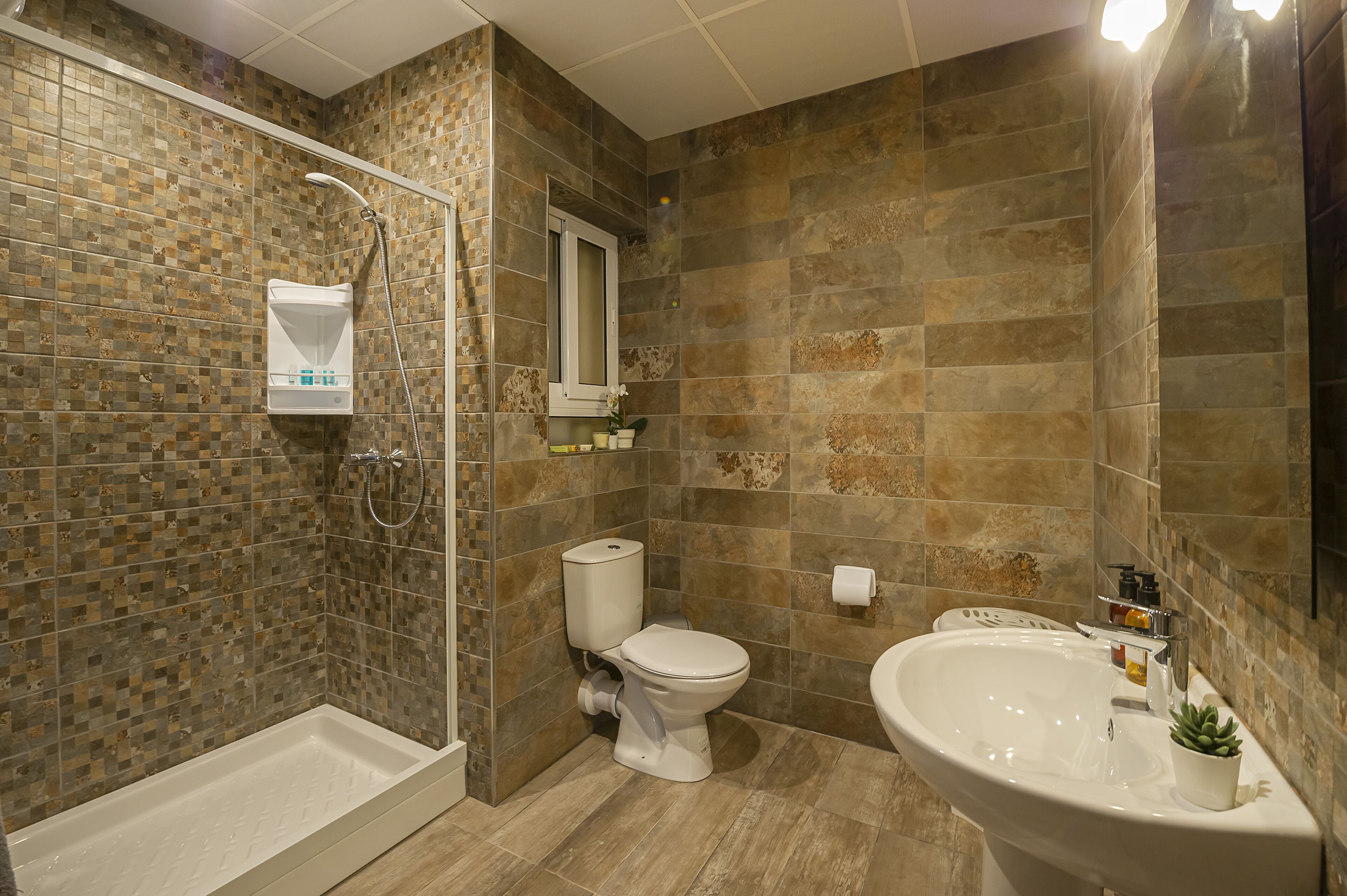 A bathroom with a shower, toilet, and sink, featuring mosaic tile walls and a modern design.