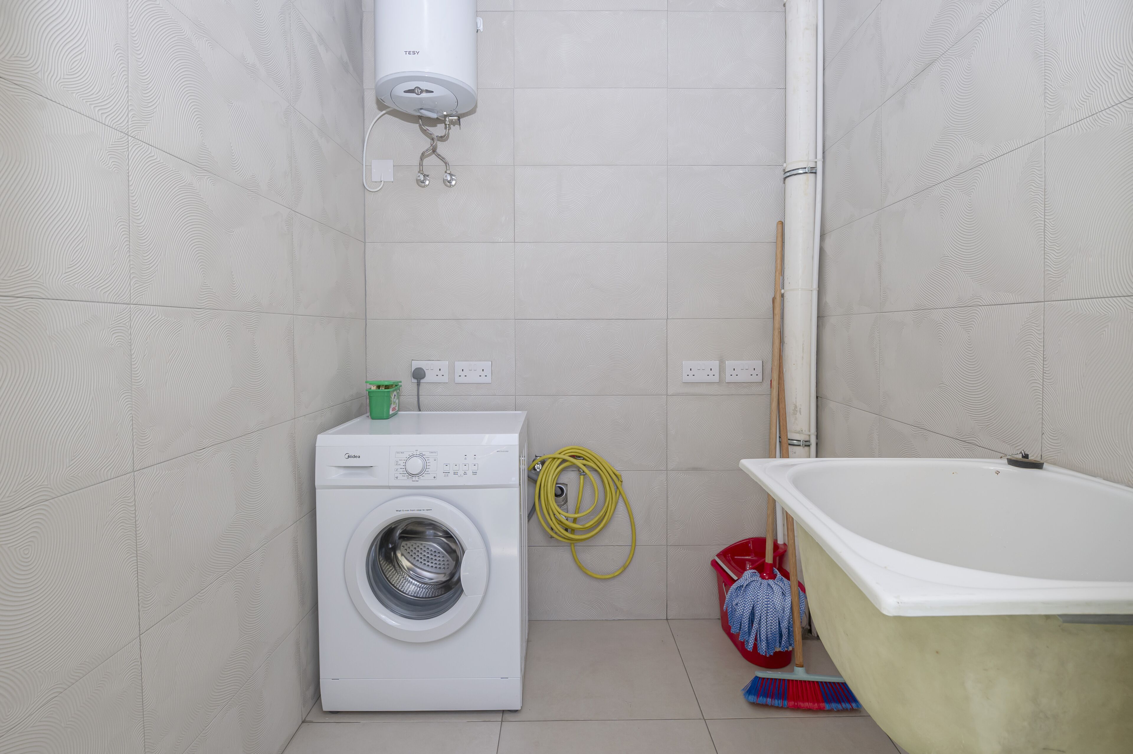 Ein Waschbereich mit Waschmaschine, Schlauch und Badewanne.