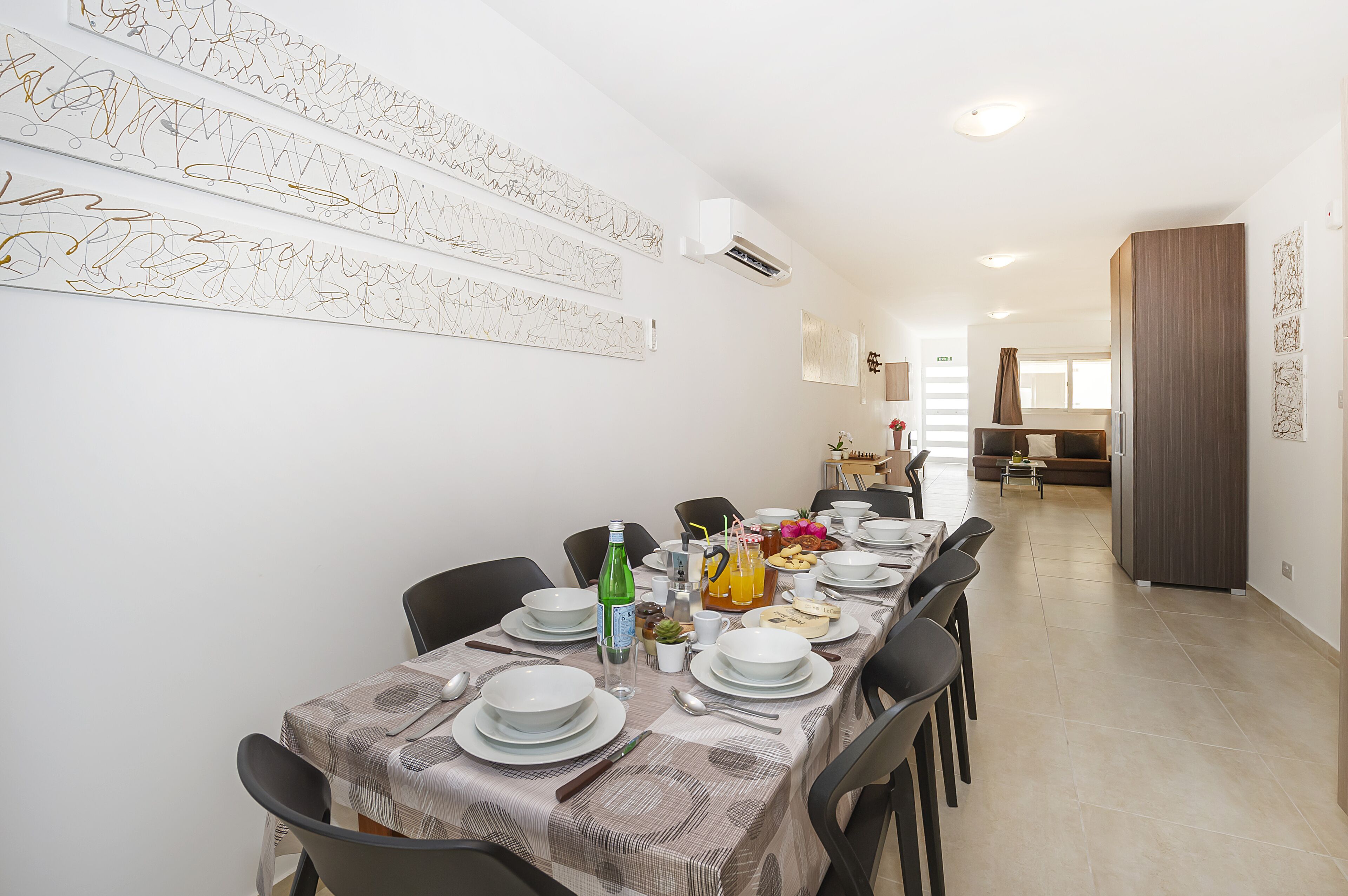 A dining area with a long table set for a meal, chairs, and a decorative wall.