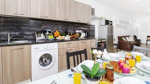 A modern kitchen with wooden cabinets, a washing machine, and a dining area with a table set for breakfast. - Summer Breeze Superior Apartment with Terrace by Getaways Malta (Mellieha)